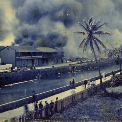 Smoke rises from burning buildings in Honolulu's Chinatown as people walk along a canal