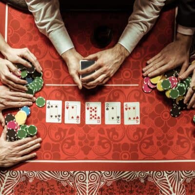 Three people playing cards with stacks of poker chips and cards spread on a red table