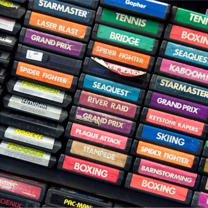 Stacked Atari game cartridges labeled with titles like Pac-Man, Frogger, and River Raid