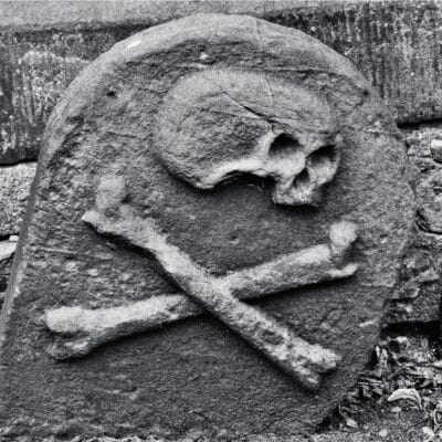 Weathered gravestone featuring a carved skull and crossbones symbol