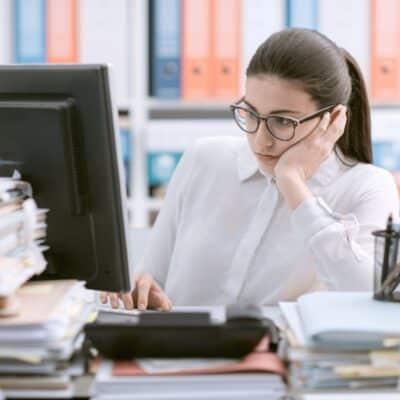 Bored office worker staring at computer with head resting on hand
