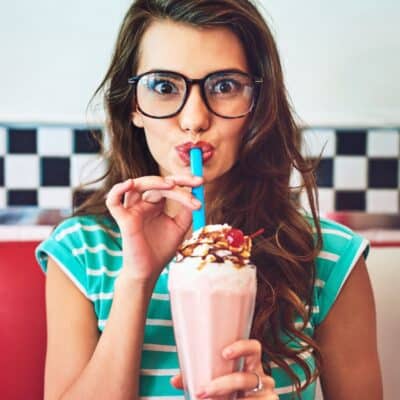 Woman sipping a strawberry milkshake topped with whipped cream and a cherry