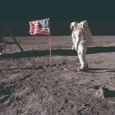 Buzz Aldrin standing on the surface of the Moon beside an American flag