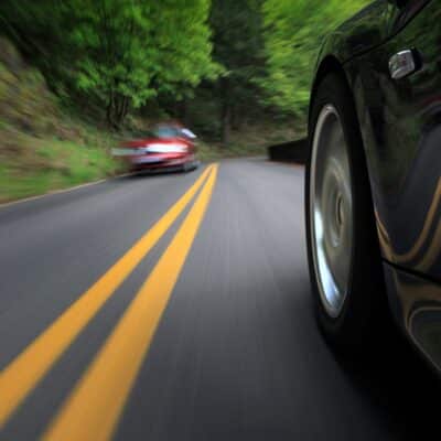 Close-up of a car speeding along a winding road toward an oncoming vehicle
