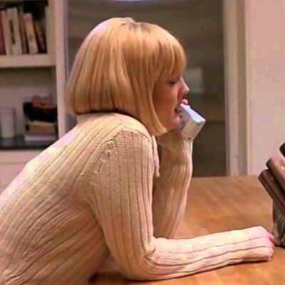 Young woman in cream sweater talking on a cordless phone in a kitchen