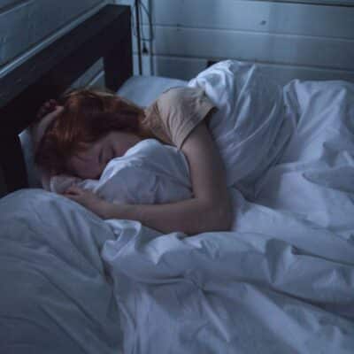 Person sleeping under white blankets in a dimly lit room
