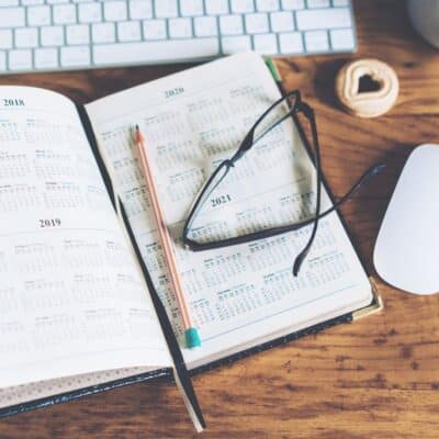 Open calendar planner with glasses, pencil, keyboard, and cookie on desk