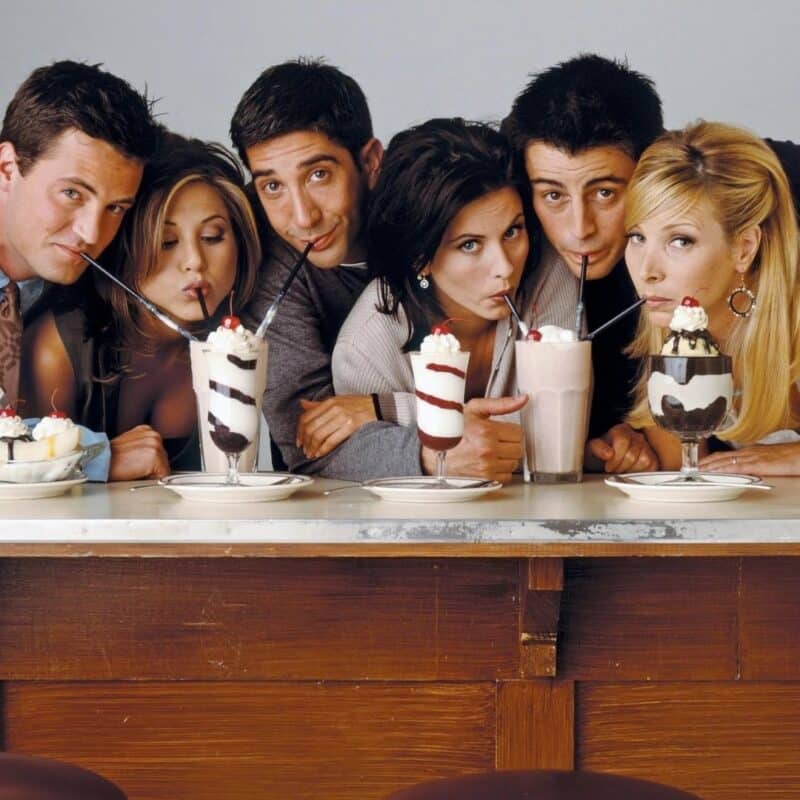 The six main Friends cast members sharing milkshakes at a diner counter