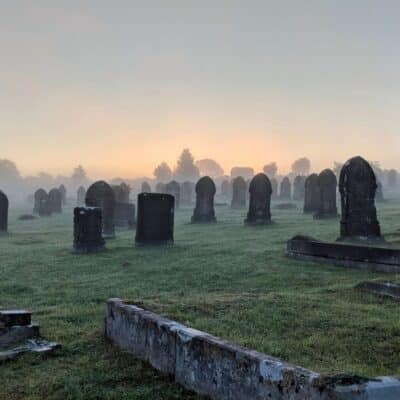 Graveyard with numerous headstones at sunrise, surrounded by a light mist