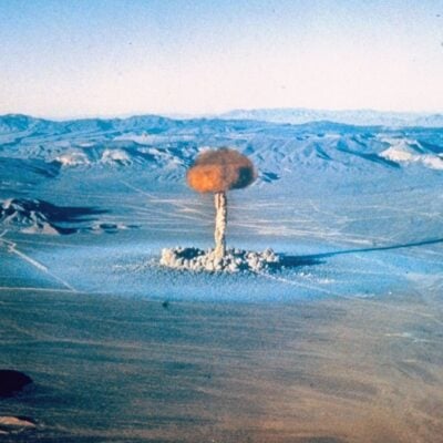 Atomic bomb explosion rises over desert landscape with mountains in the background