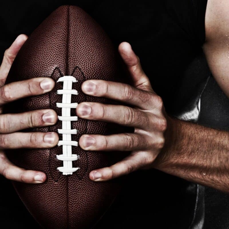 Close-up of a person holding an American football with both hands