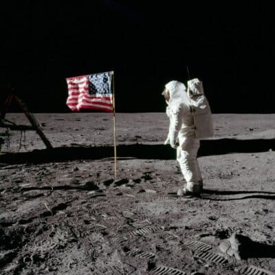 An astronaut in a white spacesuit standing on the lunar surface near an American flag