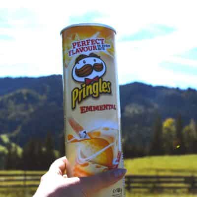 Hand holding a can of Emmental-flavored Pringles outdoors with mountains in the background
