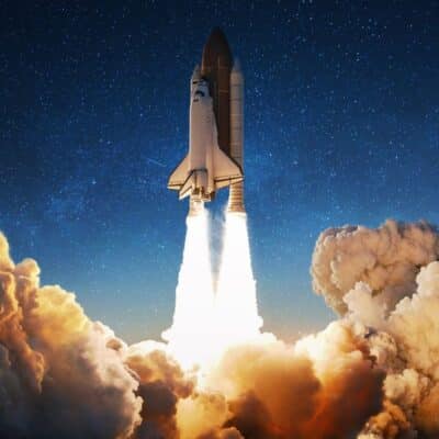 A space shuttle launching into the night sky with bright flames and smoke trailing from its boosters