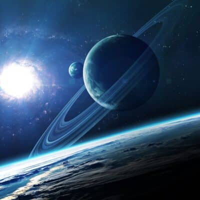 Saturn, with its prominent rings, floats in space above a brightly lit Earth