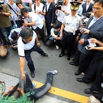 Crowd of police, media, and officials watch man reenact crime on street