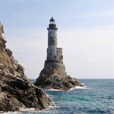 Tall, weathered lighthouse stands on rocky outcrop surrounded by ocean waves