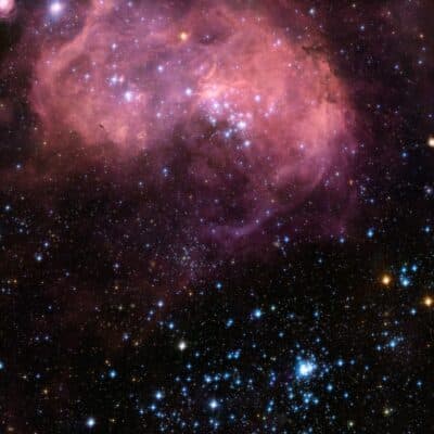 A colorful star field within a nebula, showing stars in various colors set against a pink cloud of gas and dust