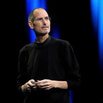 Steve Jobs wearing a black turtleneck, holding a device on stage