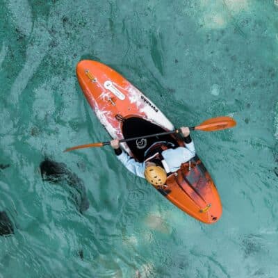 Kayaker paddling in clear turquoise water wearing a helmet and life vest
