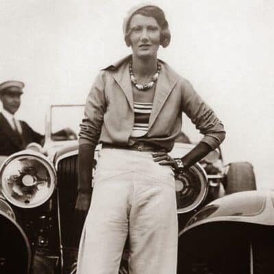 Woman in trousers standing confidently in front of a vintage car