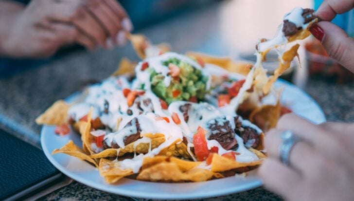 People enjoying a plate of nachos topped with cheese, meat, guacamole, and sour cream