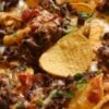 Delicious nachos topped with melted cheese, black beans, diced tomatoes, and green herbs