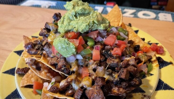Plate of nachos topped with melted cheese, diced tomatoes, grilled meat, and a dollop of guacamole