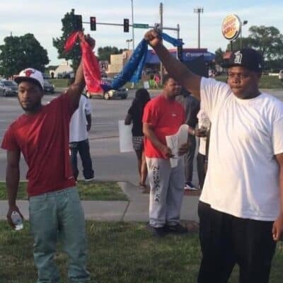 Two men hold red and blue bandanas tied together during a street demonstration