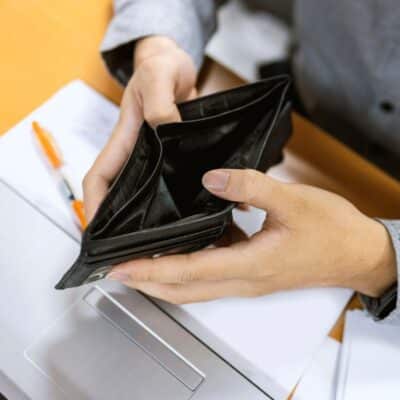Person holding an empty wallet over a laptop and documents