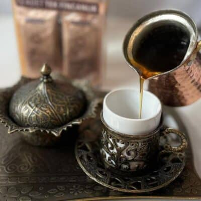 Turkish coffee being poured into an ornate cup on a decorative tray