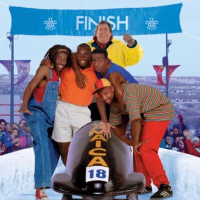 Jamaican bobsled team posing with sled at finish line, coach celebrating behind them