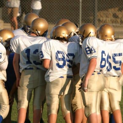 Football players in a huddle wearing white jerseys and gold helmets