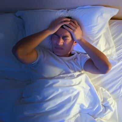 Man in bed holding his head with a pained expression