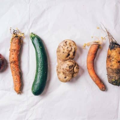 Assorted misshapen vegetables including carrots, cucumber, and potatoes on white paper