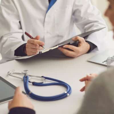Doctor taking notes during consultation with patient at desk