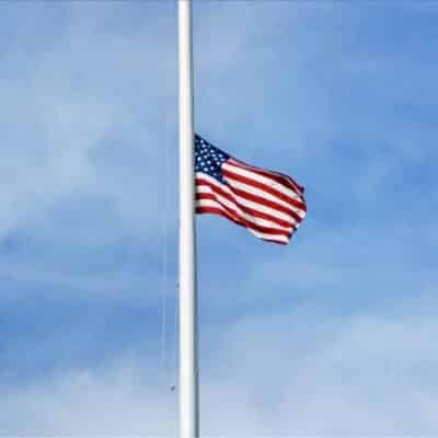 American flag flying at half-mast against a blue sky