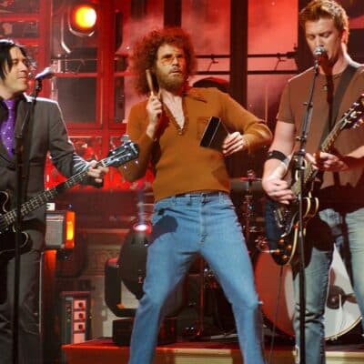 Queens of the Stone Age performing on stage with a comedic cowbell player
