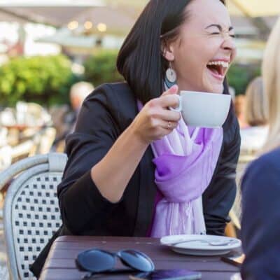 Woman laughing while holding a coffee cup at an outdoor café