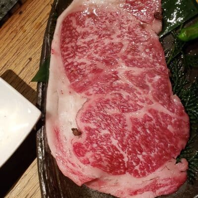 Raw marbled beef slice on a dark plate with green garnish