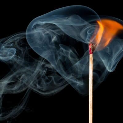 Lit matchstick with swirling smoke against a black background