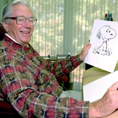 Charles Schulz smiling while holding a drawing of Snoopy