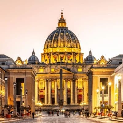 St. Peter's Basilica illuminated at dusk with people walking in front