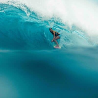 Surfer riding inside a large blue wave wearing a competition jersey