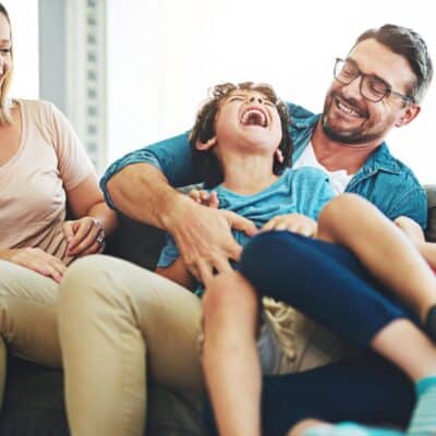 Smiling parents tickling laughing child on a couch