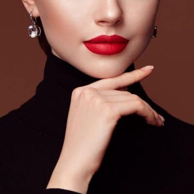 Woman wearing bold red lipstick and black turtleneck, resting hand near chin