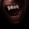 A face looming out of the darkness baring long, pointed white vampire teeth