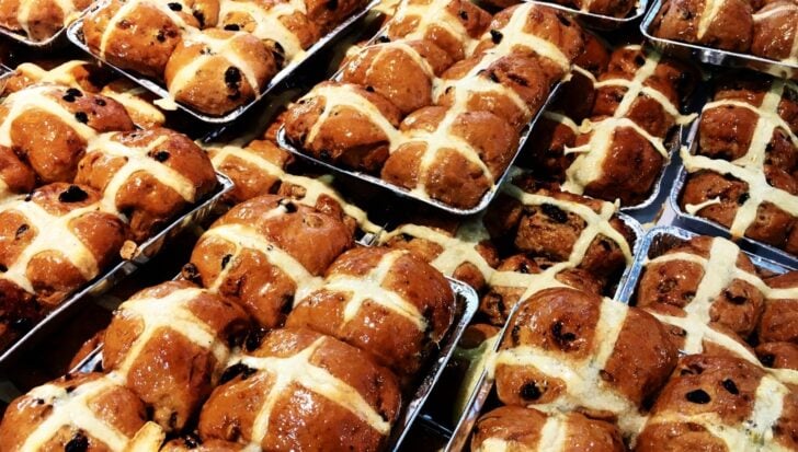 Trays of hot cross buns with raisins and a glazed topping, featuring white icing crosses