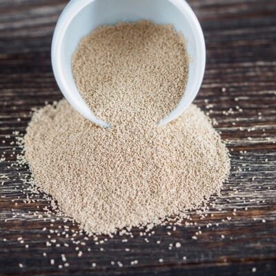Dry yeast spilling from a white container onto a wooden surface