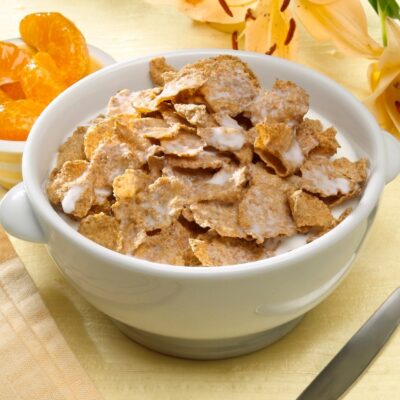 Bowl of Kellogg’s All-Bran flakes with milk next to orange slices